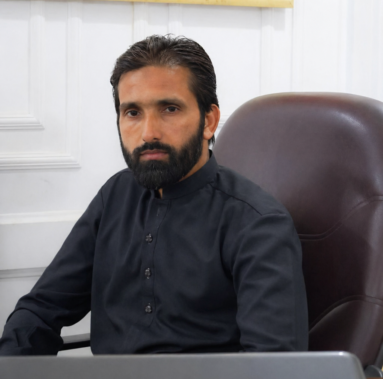 Hafiz Iqrar Ahmed sitting on a office chair